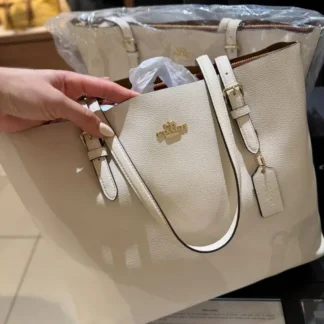 En Trendstore Chile te presentamos la Mollie Tote Bag de Coach, una cartera pensada para mujeres que buscan funcionalidad, elegancia y un diseño atemporal en un solo accesorio. Confeccionada en cuero double face de alta calidad, este modelo destaca por su combinación de tonos Gold, Chalk y Light Saddle, una paleta suave y sofisticada que aporta luminosidad y versatilidad al look. Su interior forrado en tela ofrece una experiencia cómoda y cuidada, ideal para el uso diario. Cuenta con asas largas que permiten llevarla cómodamente al hombro. Su diseño incorpora compartimentos laterales abiertos y un compartimento central con cierre superior, lo que facilita la organización de tus esenciales. En el interior incluye un bolsillo multifunción, ideal para mantener todo en orden sin perder estilo. Gracias a su formato tote, es una excelente opción para trabajo, salidas urbanas o jornadas largas, manteniendo siempre una imagen pulida y elegante. Medidas aproximadas: Largo: 41,3 cm Alto: 28,6 cm Ancho: 14 cm Caída de asas: 26 cm Materiales: Cuero double face Forro interior de tela Características principales: Modelo: Mollie Tote Bag Marca: Coach Style Number: 1671-1 Cierre superior con cremallera Compartimentos laterales abiertos Bolsillo interior multifunción Público: Mujer Un modelo original Coach, seleccionado por Trendstore para mujeres que buscan una cartera amplia, sofisticada y funcional, disponible para venta en Chile.