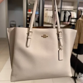 En Trendstore Chile te presentamos la Mollie Tote Bag de Coach, una cartera pensada para mujeres que buscan funcionalidad, elegancia y un diseño atemporal en un solo accesorio. Confeccionada en cuero double face de alta calidad, este modelo destaca por su combinación de tonos Gold, Chalk y Light Saddle, una paleta suave y sofisticada que aporta luminosidad y versatilidad al look. Su interior forrado en tela ofrece una experiencia cómoda y cuidada, ideal para el uso diario. Cuenta con asas largas que permiten llevarla cómodamente al hombro. Su diseño incorpora compartimentos laterales abiertos y un compartimento central con cierre superior, lo que facilita la organización de tus esenciales. En el interior incluye un bolsillo multifunción, ideal para mantener todo en orden sin perder estilo. Gracias a su formato tote, es una excelente opción para trabajo, salidas urbanas o jornadas largas, manteniendo siempre una imagen pulida y elegante. Medidas aproximadas: Largo: 41,3 cm Alto: 28,6 cm Ancho: 14 cm Caída de asas: 26 cm Materiales: Cuero double face Forro interior de tela Características principales: Modelo: Mollie Tote Bag Marca: Coach Style Number: 1671-1 Cierre superior con cremallera Compartimentos laterales abiertos Bolsillo interior multifunción Público: Mujer Un modelo original Coach, seleccionado por Trendstore para mujeres que buscan una cartera amplia, sofisticada y funcional, disponible para venta en Chile.