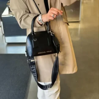 El bolso satchel pequeño de Marc Jacobs es una pieza funcional y sofisticada, pensada para mujeres que buscan estilo y comodidad en un solo accesorio. Su diseño estructurado y femenino lo convierte en un básico atemporal, fácil de combinar y perfecto para acompañarte todos los días. Confeccionado en poliuretano de alta calidad, este modelo destaca por su logo Marc Jacobs en el frontal y su cierre superior con cremallera, que mantiene tus pertenencias seguras. Gracias a su formato 2WAY, puedes llevarlo como bolso de mano tipo tote o usar la correa larga ajustable y desmontable para llevarlo cruzado, adaptándose a distintas ocasiones y estilos. El interior cuenta con un bolsillo con cierre, ideal para organizar tus esenciales como celular, billetera y llaves. En Trendstore Chile seleccionamos bolsos originales y versátiles como este Marc Jacobs, perfectos para un guardarropa moderno y funcional. Medidas y detalles – Color: Negro con detalles plateados – Material: Poliuretano (PU) – Medidas: 24 cm ancho x 10 cm profundidad x 17 cm alto – Largo de la correa: 131 cm – Caída de la correa: 69 cm – Caída de las asas: 12 cm – Uso: Tote y crossbody (2WAY) – Cierre superior con cremallera – Bolsillo interior con cierre – Logo Marc Jacobs en el frente