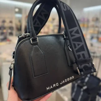 La Marc Jacobs Small Leather Dome Satchel Crossbody Bag en color negro destaca por su diseño sofisticado y femenino, ideal para acompañarte en distintas ocasiones. Confeccionada en cuero de alta calidad, presenta una estructura tipo domo que mantiene su forma y aporta un look elegante y moderno. Cuenta con cierre superior con cremallera, un bolsillo interior con cierre para organizar tus objetos y el logo Marc Jacobs en el frente, que aporta identidad al diseño. Gracias a su formato 2 en 1, puede usarse como tote con asa superior o como crossbody mediante su correa ajustable y desmontable. Sus dimensiones de 24 cm de ancho x 10 cm de profundidad x 17 cm de alto la hacen ideal para llevar tus esenciales diarios de forma cómoda y ordenada. Un bolso versátil, funcional y atemporal para uso diario o salidas especiales. Disponible en Trendstore Chile, con envío a todo el país y garantía de originalidad.