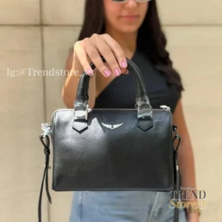 El bolso crossbody de cuero negro con detalles plateados es una opción versátil y atemporal para quienes buscan funcionalidad con un diseño elegante. Confeccionado en cuero de alta calidad, su estructura firme permite mantener la forma y organizar tus esenciales de manera cómoda y segura. Cuenta con un compartimento principal con cierre superior de cremallera, forro interior sintético y herrajes metálicos en tono plateado que aportan un acabado moderno y sofisticado. Incorpora manillas cortas de cuero para llevar en la mano y una correa larga ajustable y removible, ideal para usar cruzado o al hombro según tu estilo y ocasión. Sus dimensiones lo convierten en un bolso práctico para el uso diario, permitiendo llevar teléfono, billetera, llaves y otros básicos sin perder comodidad. Detalles del producto: – Tipo: Bolso crossbody – Color: Negro – Material: 100% cuero – Forro interior: Sintético – Cierre: Cremallera superior – Herrajes: Metálicos en tono plateado – Correa: Ajustable y removible Medidas aproximadas: – Ancho: 23 cm – Alto: 15 cm – Profundidad: 11,5 cm – Caída de asas: 10 cm – Largo máximo de correa: 51 cm Producto importado, seleccionado por Trendstore Chile para mujeres que buscan un bolso elegante, funcional y fácil de combinar, disponible para despacho a todo Chile y con todos los medios de pago.