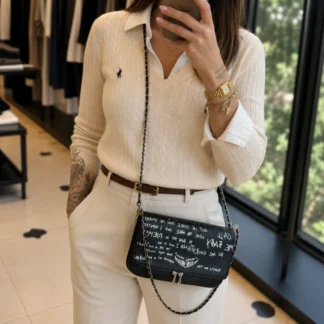 La cartera Zadig & Voltaire Rock en color negro es uno de los diseños más icónicos y reconocibles de la marca francesa. Disponible en Trendstore Chile, este modelo combina elegancia contemporánea, espíritu rockero y detalles exclusivos que la convierten en una pieza imprescindible para cualquier amante de la moda. Confeccionada en cuero de alta calidad, destaca por su sofisticado acabado negro complementado con un atractivo estampado artístico en tonos plateados que aporta personalidad y carácter al diseño. El elemento protagonista son las emblemáticas alas metálicas decoradas con delicados cristales, un sello distintivo de Zadig & Voltaire que aporta un aire moderno, femenino y sofisticado. La cadena metálica plateada permite llevarla cómodamente al hombro, añadiendo un toque elegante y versátil que funciona perfectamente tanto para el día como para la noche. Su interior espacioso permite organizar cómodamente los esenciales diarios, mientras que el bolsillo posterior con cierre proporciona almacenamiento adicional para objetos de acceso rápido. Características principales: • Diseño icónico Rock de Zadig & Voltaire • Color negro elegante y versátil • Cuero de alta calidad • Estampado artístico en tonos plateados • Emblemáticas alas metálicas con cristales • Correa de cadena metálica plateada • Interior amplio y funcional • Bolsillo trasero con cierre • Diseño ideal para uso diario o eventos especiales • Estilo rock chic parisino Beneficios: • Diseño exclusivo y reconocible • Fácil de combinar con looks casuales o elegantes • Excelente capacidad de organización • Acabados premium • Pieza icónica de la marca Gracias a su diseño sofisticado y su estética rock chic, esta cartera se convierte en el complemento perfecto para elevar cualquier outfit, desde un look casual con jeans hasta un estilismo más elegante para la noche. Disponible en Trendstore Chile, esta cartera original de Zadig & Voltaire es ideal para mujeres que buscan accesorios exclusivos, modernos y con personalidad, con compra segura y envíos a todo Chile.