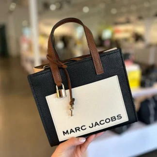 Cartera Marc Jacobs Mini CB Bold Grind Tote Black Multi original. Marc Jacobs Mini Bold Grind Tote de cuero negra disponible en Trendstore Chile. Cartera Marc Jacobs mini de cuero con charms de candado y llave. Vista frontal Marc Jacobs Mini CB Bold Grind Tote negra. Detalle de charms de candado y llave Marc Jacobs. Cartera Marc Jacobs Mini Tote con correa ajustable y desmontable. Marc Jacobs Bold Grind Tote original para mujer con envío a todo Chile. Cartera Marc Jacobs negra original disponible en Trendstore Chile.