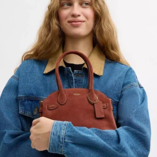 La Cartera Coach Soft Empire Carryall 21 de Gamuza y Cuero Color Clay con Brass reinterpreta la sofisticación vintage en un formato compacto y versátil. Inspirada en la actitud y el estilo de Nueva York, la colección Empire Carryall destaca por sus siluetas alargadas, materiales premium y una estética elegante que trasciende temporadas. Esta versión está confeccionada en una combinación de gamuza (suede) aterciopelada y cuero de becerro refinado, creando un atractivo contraste de texturas. El sofisticado tono Clay aporta calidez al diseño, mientras que los detalles metálicos Brass complementan la cartera con un acabado clásico y refinado. A pesar de sus dimensiones compactas, la Empire Carryall 21 está diseñada para aprovechar muy bien el espacio. Su interior incorpora un práctico bolsillo multifunción con broche para organizar pequeños esenciales y hebillas interiores que permiten expandir los fuelles laterales cuando necesitas un poco más de capacidad. El cierre superior completo con cremallera mantiene tus pertenencias protegidas. Sus dos asas estructuradas permiten llevarla elegantemente en la mano, mientras que la correa larga desmontable ofrece la posibilidad de usarla al hombro o como crossbody para mantener las manos libres. Además, incorpora cuatro apoyos protectores en la base, un detalle especialmente práctico para ayudar a proteger el cuero y la gamuza cuando apoyas la cartera sobre diferentes superficies. En Trendstore Chile encontrarás productos 100% originales Coach, cuidadosamente seleccionados para ofrecer diseños premium, exclusivos y difíciles de encontrar en Chile, con compra segura y envíos a todo el país. La Coach Soft Empire Carryall 21 Clay es ideal para mujeres que buscan una cartera compacta con materiales de lujo, personalidad y múltiples formas de uso. Materiales: Exterior de gamuza aterciopelada. Detalles en cuero de becerro refinado. Forro interior de tela. Herrajes en acabado Brass. Características: Modelo Soft Empire Carryall 21. Diseño de inspiración vintage. Combinación de gamuza y cuero refinado. Color Clay con detalles Brass. Dos asas superiores. Correa larga desmontable para hombro o crossbody. Bolsillo interior multifunción con broche. Hebillas interiores para expandir los fuelles laterales. Cierre superior con cremallera. Cuatro apoyos protectores en la base. Style Number: CEC03. Medidas: Largo: 20,3 cm Alto: 17,1 cm Ancho: 12,7 cm Caída de las asas: 13,3 cm Caída de la correa desmontable: 54,6 cm