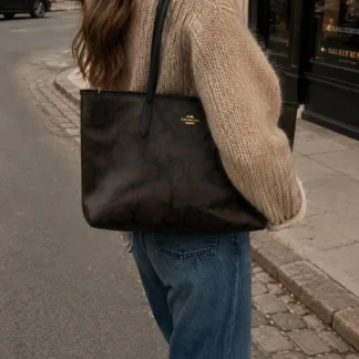 Cartera Coach Large City Tote Maxi Signature Canvas Gold Walnut Black original disponible en Trendstore Chile. Vista frontal de la Coach Large City Tote con monograma Maxi Signature y compra segura en Chile. Detalle del Signature Coated Canvas de la cartera Coach Large City Tote original en Trendstore Chile. Vista lateral de la Coach Large City Tote Walnut Black de gran capacidad con envío a todo Chile. Interior de la cartera Coach Large City Tote con bolsillo y cierre de cremallera disponible en Trendstore Chile. Cartera tote Coach Maxi Signature original para mujer, modelo amplio premium con despacho a todo Chile. Detalle del monograma Maxi Signature y terminaciones de la Coach Large City Tote original en Trendstore Chile. Coach Large City Tote Gold Walnut Black original con compra segura y envío a todo Chile desde Trendstore Chile.